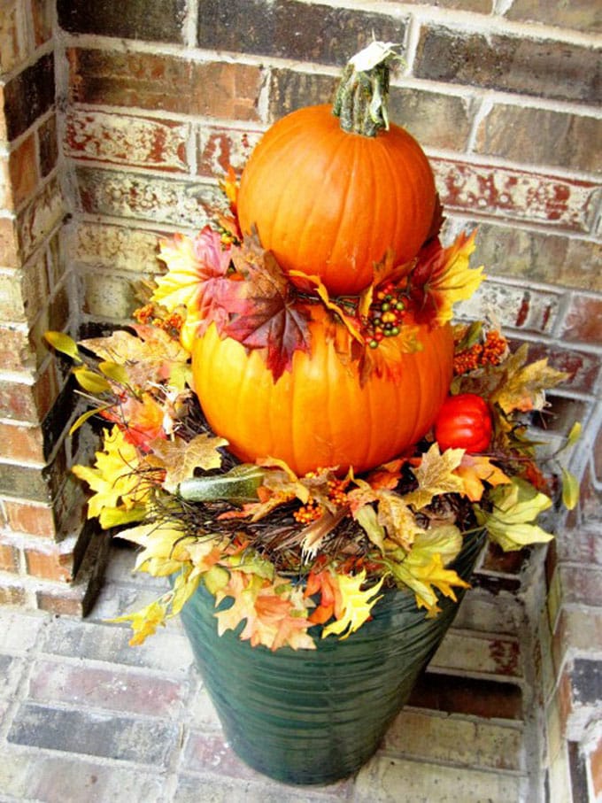 place vibrant fall leaves in a planter with stacked pumpkins for easy and colorful DIY fall outdoor decorations