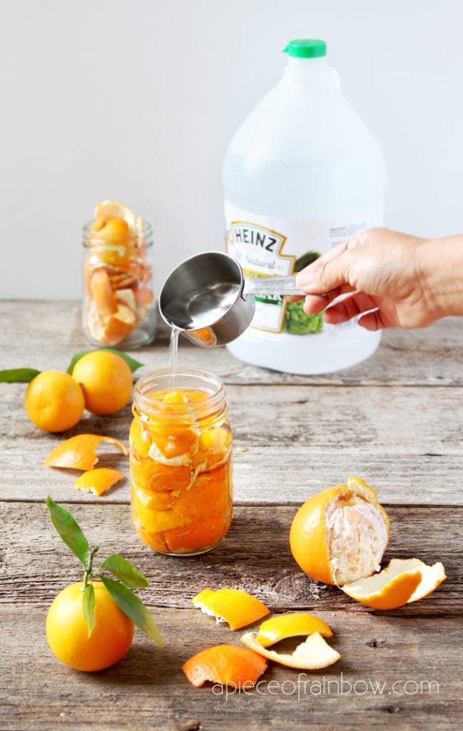 pouring white vinegar into jar with orange peels