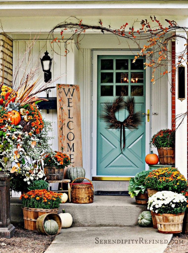 beautiful fall porch: potted mums, kale, pumpkins,  garlands made out of vines and branches, and a fall welcome sign