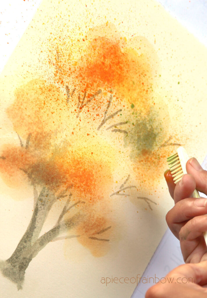 Create watercolor splatters using a toothbrush